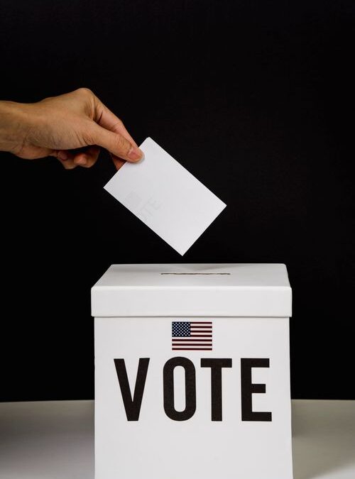 Mano depositando una boleta en una urna marcada 'Vote' con la bandera de Estados Unidos