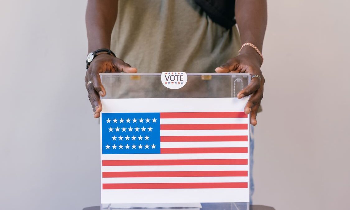 Persona depositando su voto en una urna transparente con la bandera de Estados Unidos