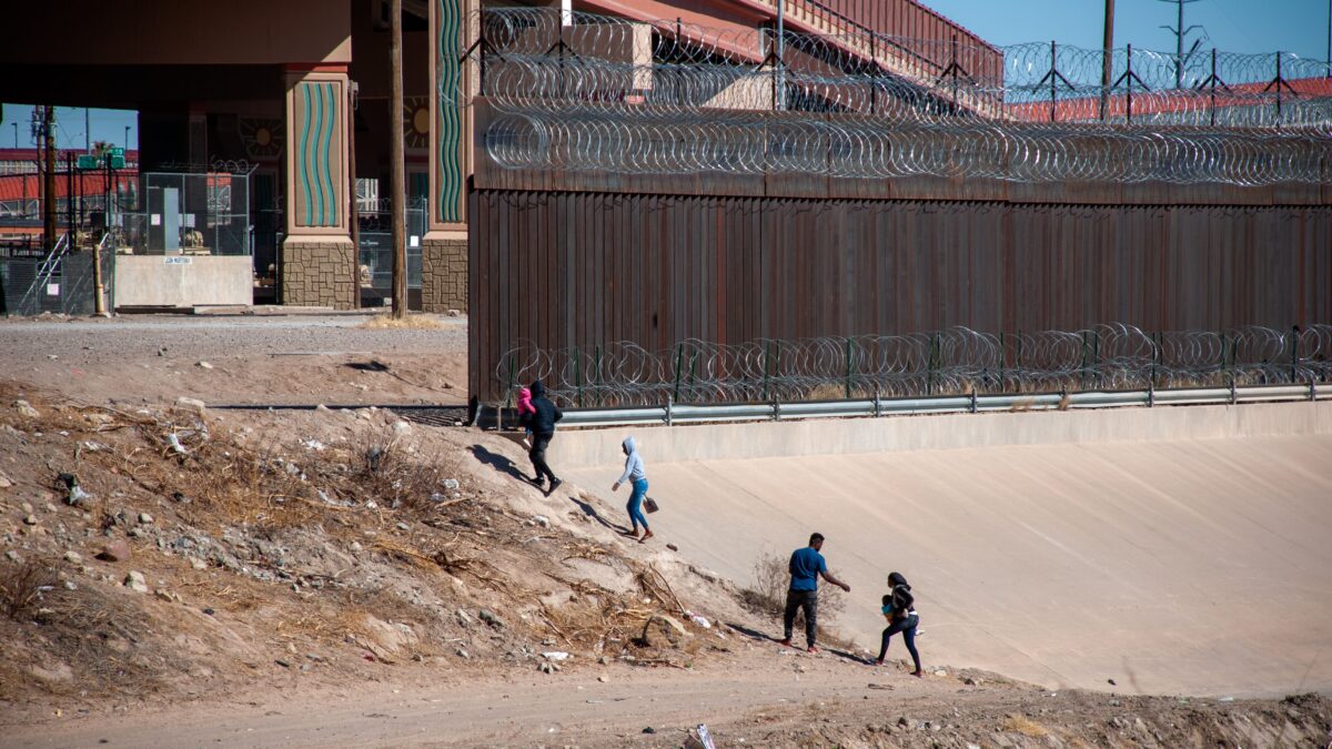 Border wall between Mexico and the United States with barbed wire and migrants crossing