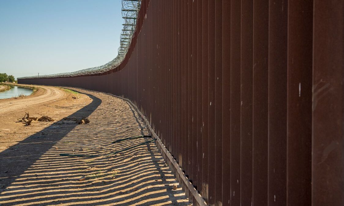 Muro fronterizo de acero visto a lo largo de un camino de tierra bajo un cielo despejado