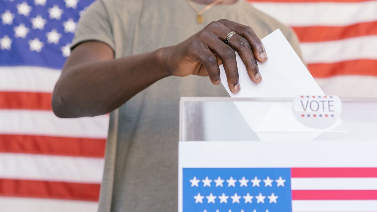 Persona depositando su voto en una urna con la bandera de Estados Unidos de fondo