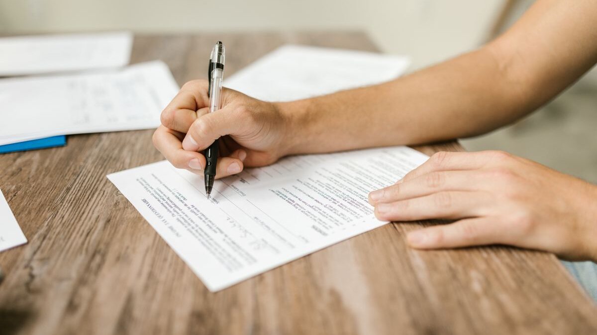 Close-up of a hand filling out an immigration paperwork form with a pen