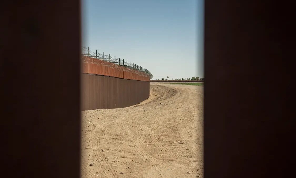 Muro fronterizo de acero con alambre de púas junto a un camino de tierra en el desierto. Foto de Mark Stebnicki en Pexels