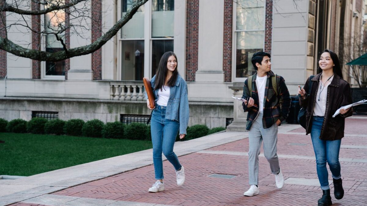 Estudiantes universitarios caminando por el campus con libros y mochilas