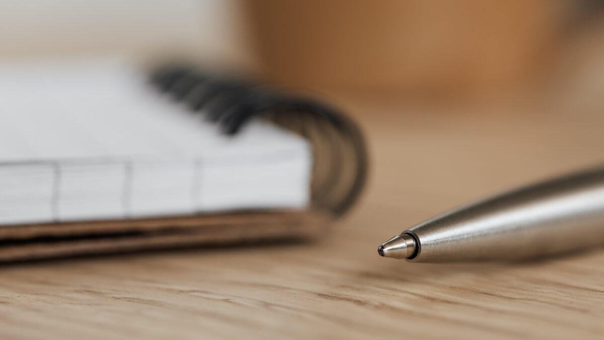 Cuaderno en blanco con un bolígrafo plateado sobre un escritorio de madera