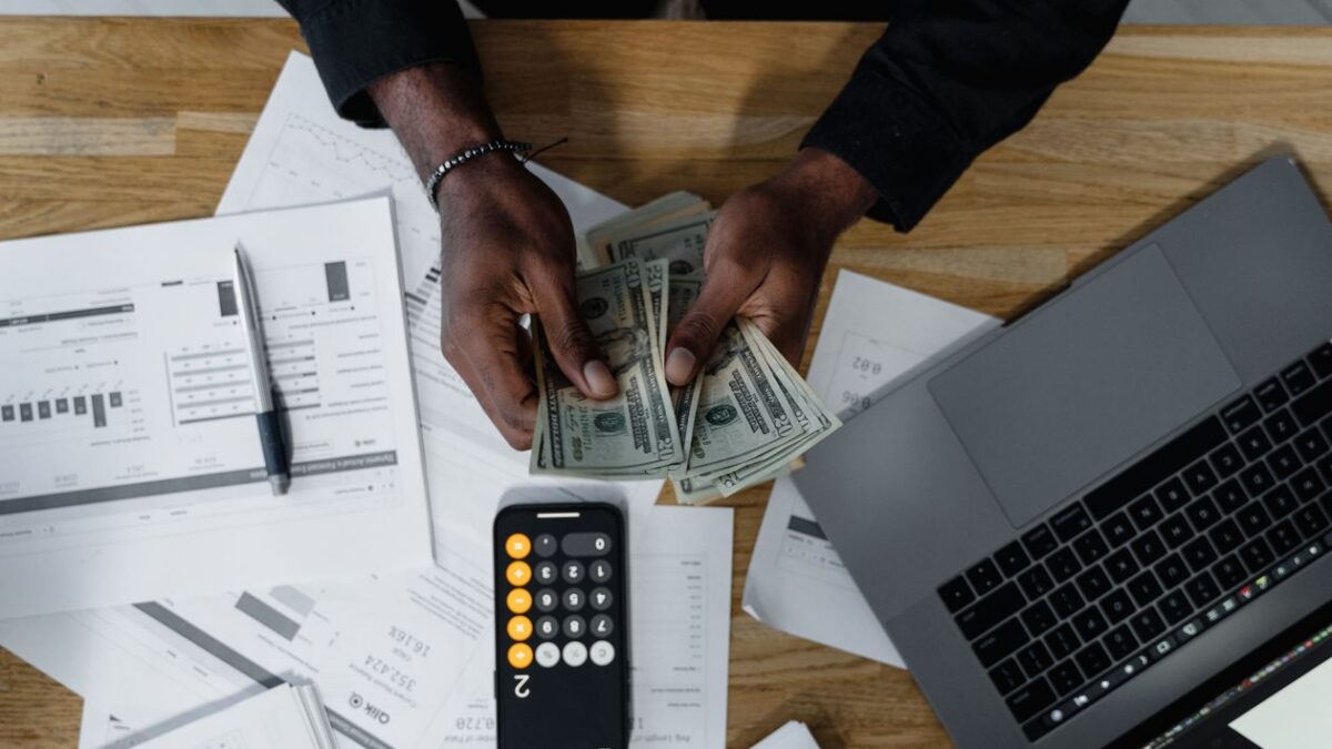 Persona contando dólares con una calculadora y documentos financieros