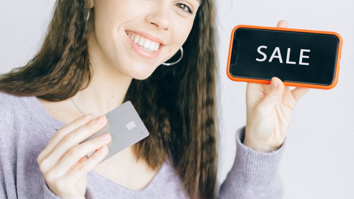 Mujer revisando su celular con una tarjeta bancaria en la mano